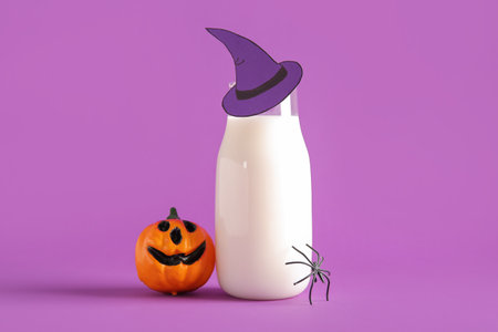 Bottle of milk, hat made of paper, pumpkin and spider for Halloween on purple backgroundの写真素材