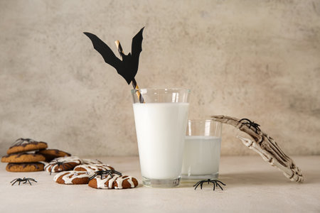 Glasses of milk, bat, skeleton hand and tasty cookies for Halloween on light backgroundの写真素材