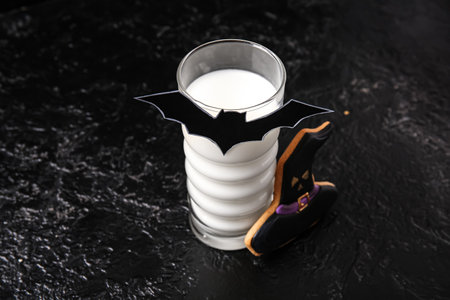 Glass of milk, bat made of paper and tasty cookie for Halloween on dark background, closeupの写真素材