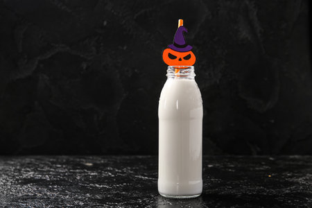 Bottle of milk and pumpkin made of paper for Halloween on dark backgroundの写真素材