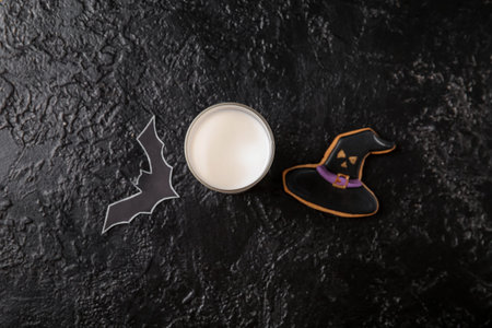 Glass of milk, bat and tasty cookie for Halloween on dark backgroundの写真素材