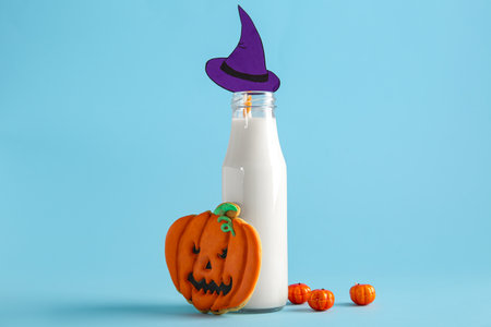 Bottle of milk, tasty cookie and hat made of paper for Halloween on blue backgroundの写真素材