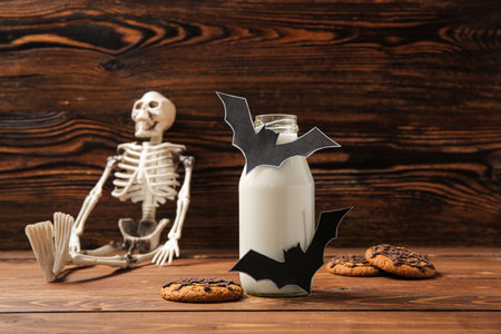 Bottle of milk, skeleton, tasty cookies and bats made of paper for Halloween on wooden backgroundの写真素材