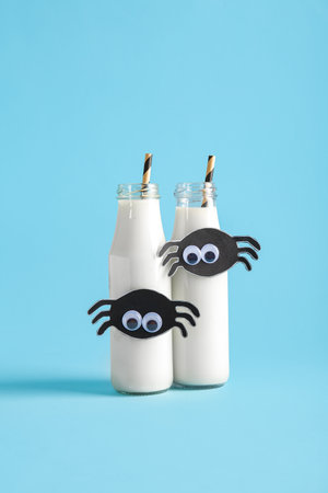 Bottles of milk and spiders made of paper for Halloween on blue backgroundの写真素材