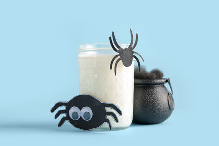 Glass of milk, bowl and spiders for Halloween on blue background, closeupの写真素材