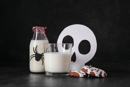 Tasty cookies, skull made of paper, bottle and glass of milk for Halloween on dark background, closeupの写真素材