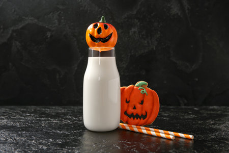 Bottle of milk, straws and tasty cookie for Halloween on dark backgroundの写真素材