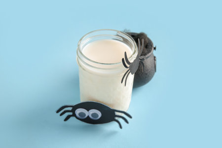 Glass of milk, bowl and spiders for Halloween on blue background, closeupの写真素材