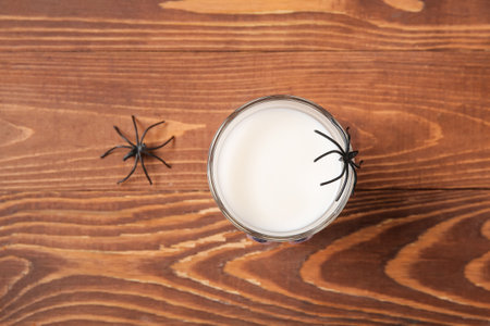 Glass of milk and spiders for Halloween on wooden backgroundの写真素材