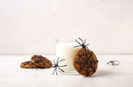 Glass of milk, tasty cookies and spiders for Halloween on light background, closeupの写真素材