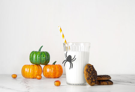 Glass of milk, tasty cookies and pumpkins for Halloween on light backgroundの写真素材
