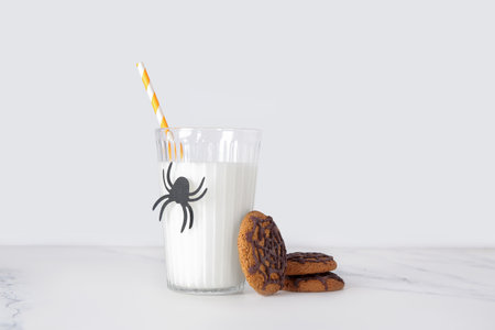 Glass of milk, spider and tasty cookies for Halloween on light backgroundの写真素材