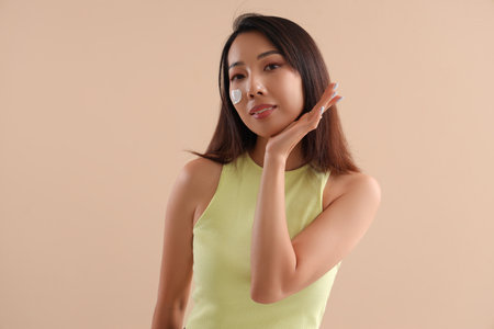 Beautiful Asian woman with cream on her face against beige backgroundの写真素材