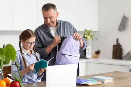Father helping his little daughter to pack schoolbag in kitchenの写真素材
