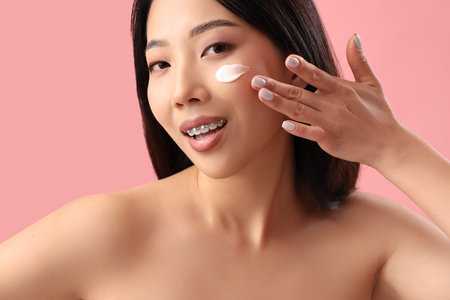 Beautiful Asian woman with cream on her face against pink backgroundの写真素材