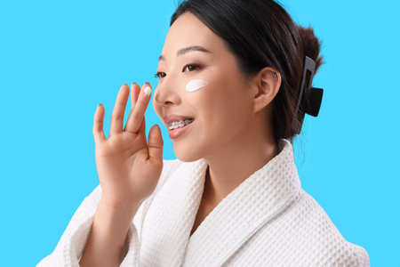 Beautiful Asian woman with cream on her face against blue backgroundの写真素材