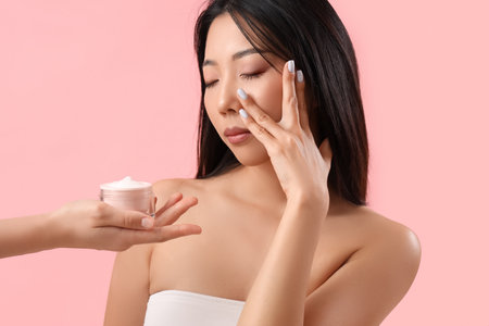 Beautiful Asian woman and hand with cream on pink backgroundの写真素材