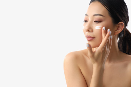 Beautiful Asian woman applying facial cream against white backgroundの写真素材