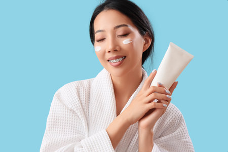 Beautiful Asian woman with facial cream on blue backgroundの写真素材