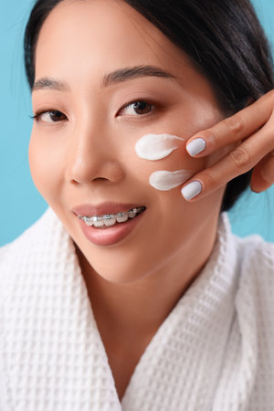 Beautiful Asian woman with cream on her face against blue backgroundの写真素材
