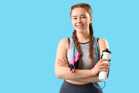 Sporty young woman with skipping rope and bottle of water on blue backgroundの写真素材