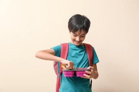 Little schoolboy with lunchbox on beige backgroundの写真素材
