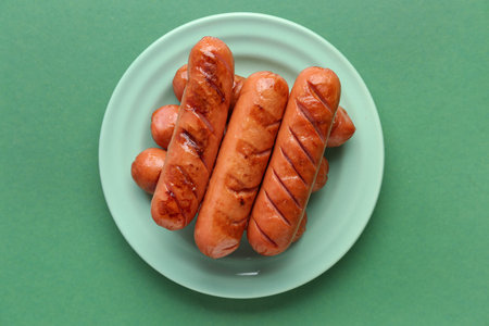 Plate with tasty grilled sausages on green backgroundの写真素材