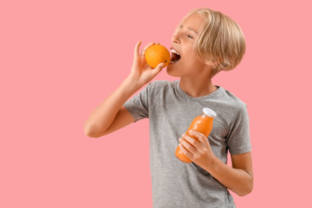 Little boy with bottle of juice eating orange on pink backgroundの写真素材