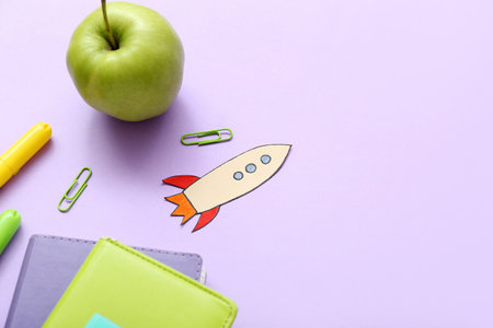 Paper rocket with school stationery and apple on purple backgroundの写真素材