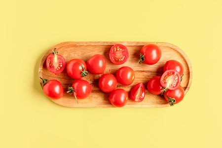 Wooden board with fresh cherry tomatoes on yellow backgroundの写真素材