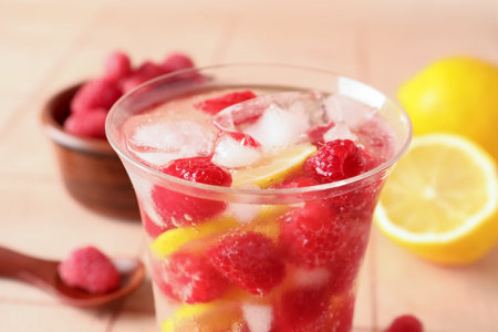 Glass of fresh raspberry lemonade and bowl with berries on pink tile table