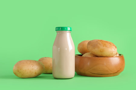Bottle of tasty potato milk and fresh vegetables on green backgroundの写真素材