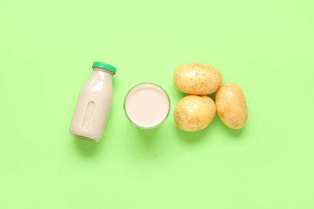 Bottle and glass of tasty potato milk with fresh vegetables on green backgroundの写真素材