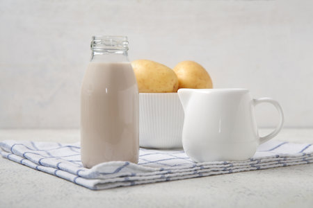 Bottle and jug of tasty potato milk on light backgroundの写真素材