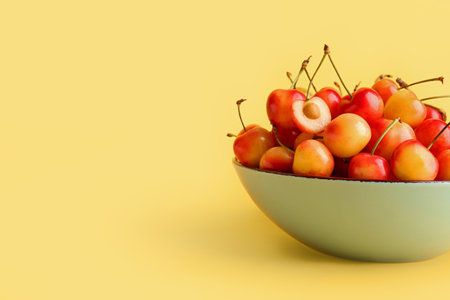 Bowl with sweet yellow cherry on color backgroundの写真素材