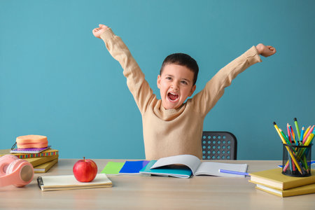 Happy little boy doing homework at table near blue wallの写真素材