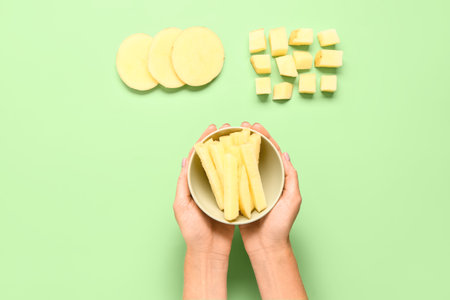 Woman holding bowl with pieces of raw potato on green backgroundの写真素材