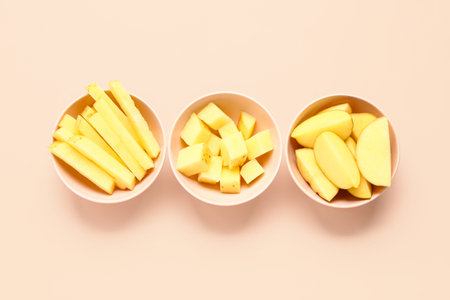 Bowls with pieces of raw potato on pink background