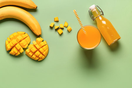 Glass and bottle of fresh mango juice with bananas on green backgroundの写真素材