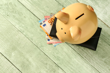 Piggy bank with euro banknotes and wallet on green wooden backgroundの写真素材