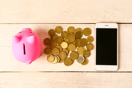Piggy bank with coins and mobile phone on light wooden backgroundの写真素材