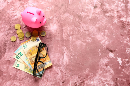 Piggy bank with money and eyeglasses on grunge pink backgroundの写真素材