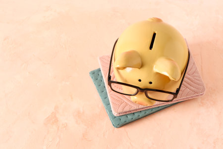 Piggy bank in eyeglasses with books on grunge pink backgroundの写真素材