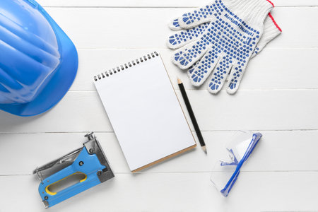 Composition with notebook, building stapler, hardhat and gloves on white wooden background. labor day celebrationの写真素材