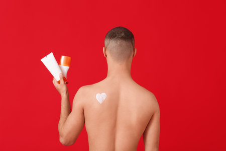Young man with bottles of sunscreen cream on red background, back viewの写真素材