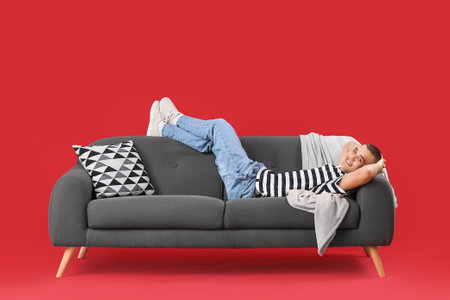 Happy young man lying on sofa against red backgroundの写真素材
