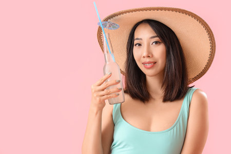 Beautiful Asian woman in swimsuit and with drink on pink backgroundの写真素材