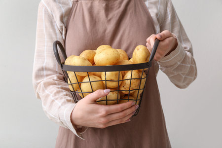 Woman holding basket with raw potatoes on light backgroundの写真素材