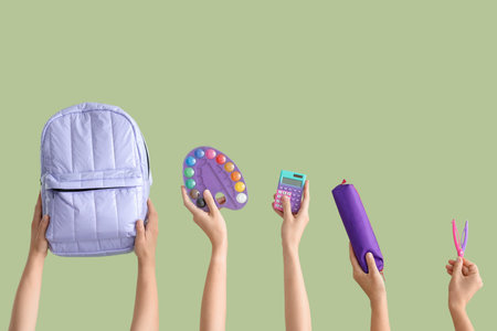 Female hands with backpack and different stationery on green backgroundの写真素材