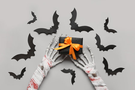Skeleton hands with gift box and paper bats for Halloween celebration on gray backgroundの写真素材